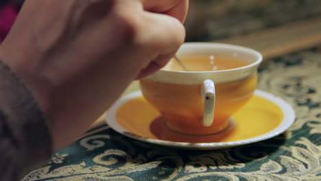 Hand-Nimmt-Löffel-Und-Rührt-Tee-Zum-Trinken-Aus-Verzierter-Teetasse,-Nahaufnahme