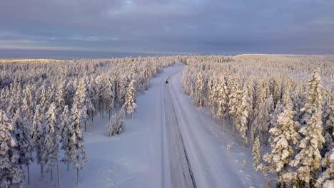 Forward-aerial-above-snowy-Winter-Road,-Car-driving-in-distance