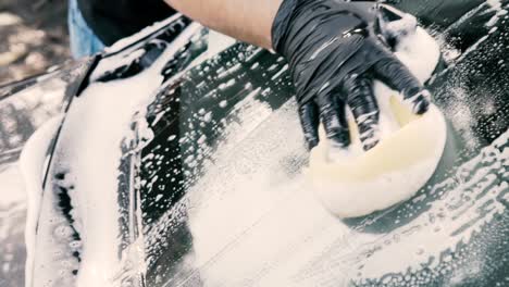 Nahaufnahme-Eines-Mannes,-Der-Ein-Auto-Mit-Schwarzen-Handschuhen-Mit-Shampoo-Und-Schwamm-Wäscht