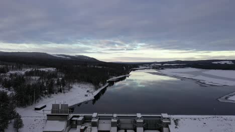Dreamlike-pull-back-aerial-over-mirror-reflection-in-lake,-reveal-dam,-forest-winter-landscape,-asendammen,-Sweden