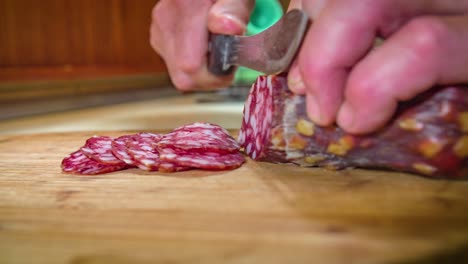 Hands-hold-salami-while-being-sliced-up-on-wooden-cutting-board