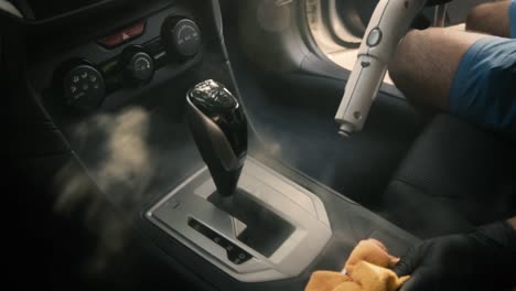 Male-wearing-black-gloves-cleaning-car-shift-lever-area-with-steam