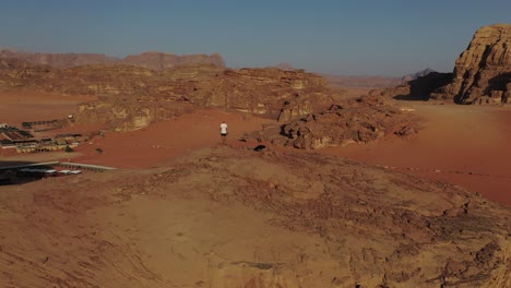 Climber-overlooking-Wadi-Rum-landscape-on-top-of-mountain,-drone-arc-shot
