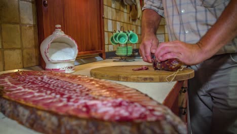 Man-hand-cut-salami-by-knife-on-wooden-board,-Slovenia,-closeup-slowmo