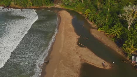 Revealing-aerial-of-a-river-flowing-into-the-sea-with-a-rainforest-in-the-background-at-Grande-Riviere-Beach,-Trinidad