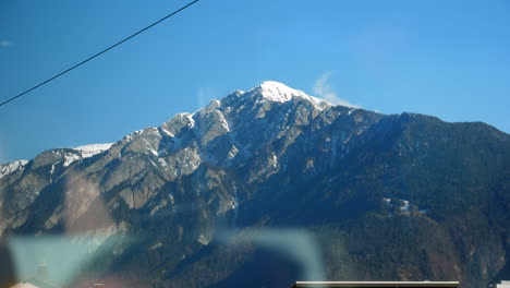Vista-Del-Viaje-En-Tren-Expreso-Glaciar-Con-Reflejo-De-Ventana-Y-Mezcla-De-Viviendas-Rurales-Y-Montañas