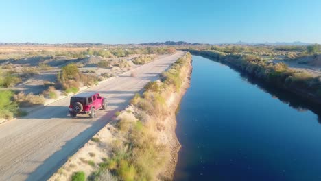 Schließen-Sie-Die-Luftaufnahme-Von-Einem-Roten-Geländewagen,-Der-Auf-Der-Straße-In-Der-Nähe-Des-Gila-Gravitationsbewässerungskanals-Fährt---Yuma,-Arizona