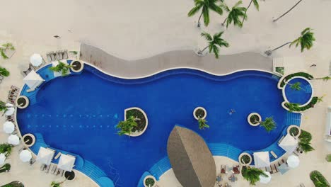 Luxus-Ferienresort-Mit-Swimmingpool,-Luxus-Terrasse-Mit-Liegestühlen-Und-Sonnenschirmen-Neben-Tropischem-Sandstrand-Mit-Palmen,-Gehobenes-Romantikhotel,-Luftbild-Von-Oben-Nach-Unten