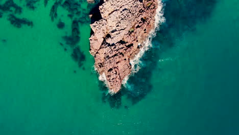 AERIAL:-looking-down-on-a-point-rock-formation-with-crystal-clear-water