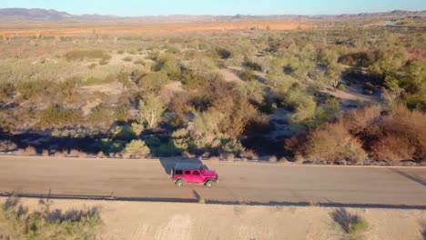 Aerial-view-of-red-SUV-driving-through-Mittry-Wildlife-Refuge-and-past-a-spillway--Yuma,-Arizona