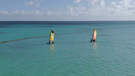 Two-small-catamarans-sail-in-turuoise-Caribbean-Sea,-watersport-fun-and-recreatin-in-tropical-paradise