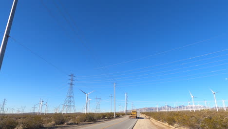 Parked-on-the-side-of-the-road-in-the-Mojave-desert-in-California-with-a-trailer-truck-passing-by-with-windmills-and-power-lines-in-the-distance---Wide-shot