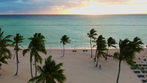 Tropical-sand-beach-with-palm-trees,-deckchairs-and-turquoise-water-in-sunset,-sunrise,-Dominican-Republic,-Punta-Cana,-aerial-view