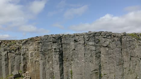Basalt-columns-rock-wall-revealing-mountains-in-background-Iceland