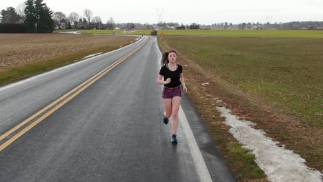 Running-teenage-girl,-attractive-young-woman,-slow-motion-jogger-on-empty-country-road-in-winter-with-snow,-race-training