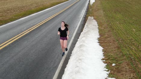 Female-runner-tracking-shot,-close-up-of-teenage-girl-exercising,-cardio-activity,-snow-along-side-of-road-in-Pennsylvania-USA,-slo-mo