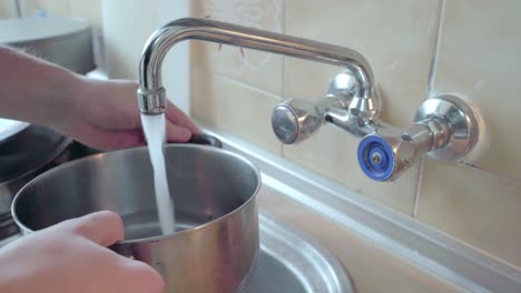 Hand-opening-faucet,-pouring-water-in-kettle