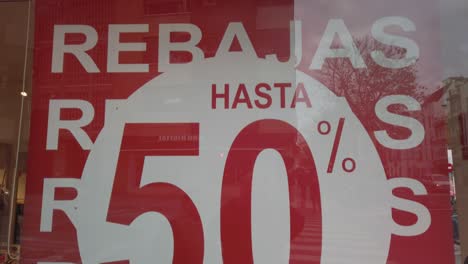 Tilt-Up-of-Half-Off-Sale-Sign-in-Shop-Window-with-Spanish-Rebajas-Writing