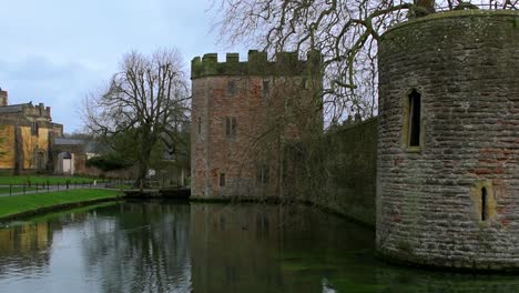 Over-the-moat,-looking-towards-the-imposing-walls-and-castle-towers-of-the-Medieval-Bishop's-Palace-in-Well,-UK