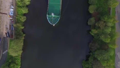 Aerial-drone-shot-top-down-over-water-a-ship-passes-green-landscape-and-environment