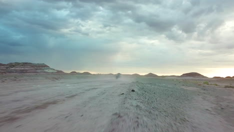 Dynamic-Tracking-Aerial-View-of-ATV-Vehicle-Moving-Fast-on-Dusty-Road-in-Dry-Deset-Landscape-Under-Dramatic-Sky