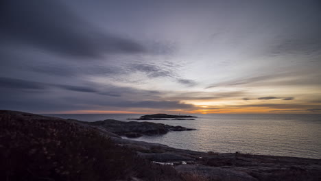 Time-lapse-clouds-move-toward-rising-sun-over-ocean-with-rocky-shore