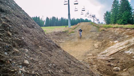 Mountain-biker-rides-downhill-towards-camera,-preparing-for-jump