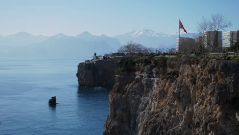 Full-shot,-Antalya-Cliff,-tourist-boat-sailing-on-the-sea,-toros-mountain-in-turkey-in-the-background