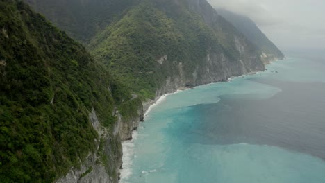 Qingshui-lush-cliffs-cloudy-peaks-aerial-view-slow-tilt-up-from-seascape-Taroko-gorge-Hualien-County-shoreline
