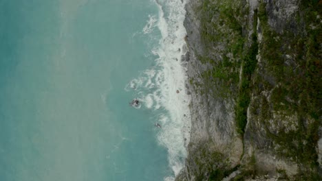 Aerial-birds-eye-view-overlooking-cliff-edge-rock-face---breaking-coastal-ocean-waves-splashing-against-rocky-shoreline