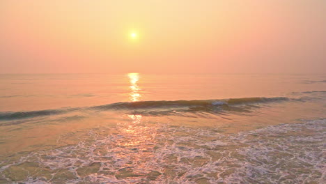 Slow-motion-shot-of-orange-and-peach-sunrise-over-ocean-with-breaking-waves