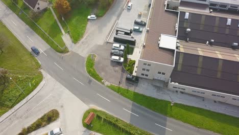 A-cinematic-view-of-car-crossing-the-road-from-the-top-zooming-in-with-an-industry-roof-top-and-vehicles-parked