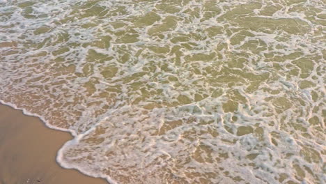 Close-up,-slow-motion-shot-of-small-waves-breaking-on-sandy-beach,-warm-light