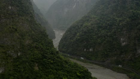 Aerial-tilt-up-across-winding-tropical-woodland-river-greenery-to-Taroko-Valley-mountain-wilderness-layers---cloudy-peaks