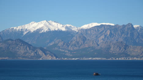 Turkish-fishing-boat-slowly-crossing-the-Mediterranean-Sea-with-snow-covered-mountains-visible