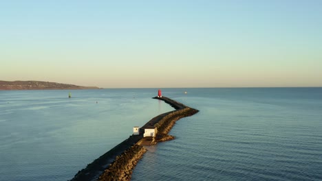 Aerial-dolly-in-at-Dublin-sea-wall-at-sunset,-Poolbeg-lighthouse-in-background
