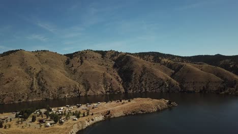 Aerial-view-of-an-RV-campground-site-in-Montana-with-mountains,-river-and-boats-in-the-background