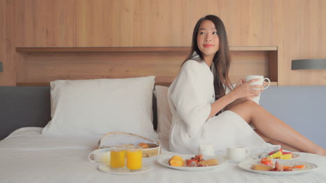 Young-woman-in-bathrobe-enjoying-breakfast-in-bed