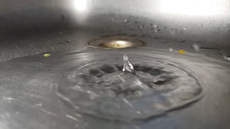 Faucet-drainage-hole-in-stainless-kitchen-sink-with-water-dripping-and-splashing-droplets-in-slow-motion