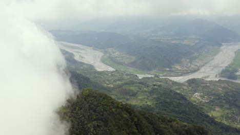 High-altitude-aerial-view-above-Dulan-mountain-peak-over-clouds-to-vast-cultivated-farmland-below-in-Taitung-valley