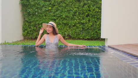 Asiatische-Frau,-Die-In-Einem-Resort-Infinity-Pool-Mit-Hut-Sitzt
