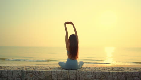 Ein-Junges-Mädchen,-Das-Yoga-Am-Strand-Praktiziert,-Während-Es-Bei-Sonnenuntergang-Auf-Das-Meer-Blickt