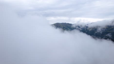 Drone-flying-over-a-thin-layer-of-clouds-towards-a-mountain-landscape