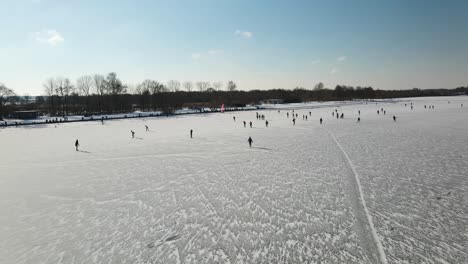 Drone-shot-Of-Ice-Skating-People-Outdoors-on-natural-frozen-lake-during-winter---Sun-reflecting-on-ice-layer---Loosdrecht,Netherlands