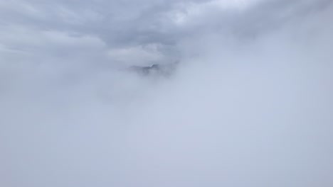 Drone-passing-through-white-static-high-clouds-where-mountain-range-appears-on-the-horizon