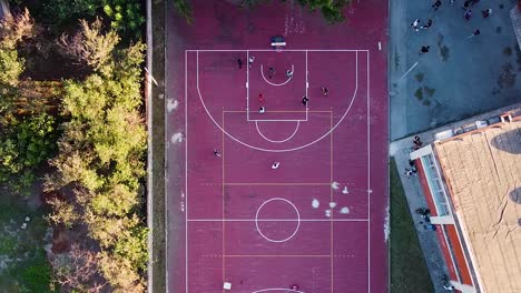 Drone-view-of-some-people-playing-basketball-in-an-open-court,-surrounded-by-trees