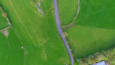 Static-aerial-drone-shot-looking-down-as-a-single-motor-car-drives-a-country-lane-in-Summer