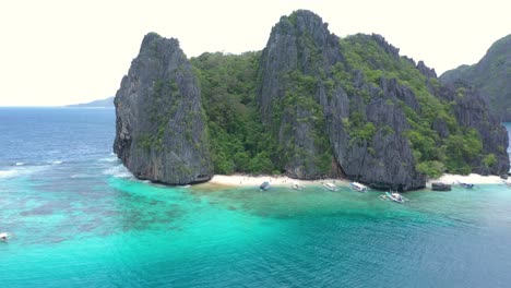 Drone-flying-backwards-from-beautiful-white-sand-secret-beach-with-huge-limestone-cliffs,-turquoise-water,-and-natural-archipelago-paradise-in-El-Nido,-Palawan,-Philippines