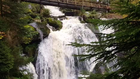 Statische-Nahaufnahme-Des-Wunderschönen-Massiven-Triberger-Wasserfalls-Unter-Holzbrücke-Während-Der-Herbstsaison,-Schwarzwald-Schwarzwald,-Deutschland