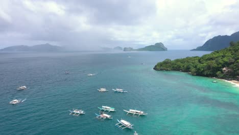 Drone-circling-around-huge-limestone-cliffs,-turquoise-water,-small-boats-and-natural-archipelago-paradise-in-El-Nido,-Palawan,-Philippines